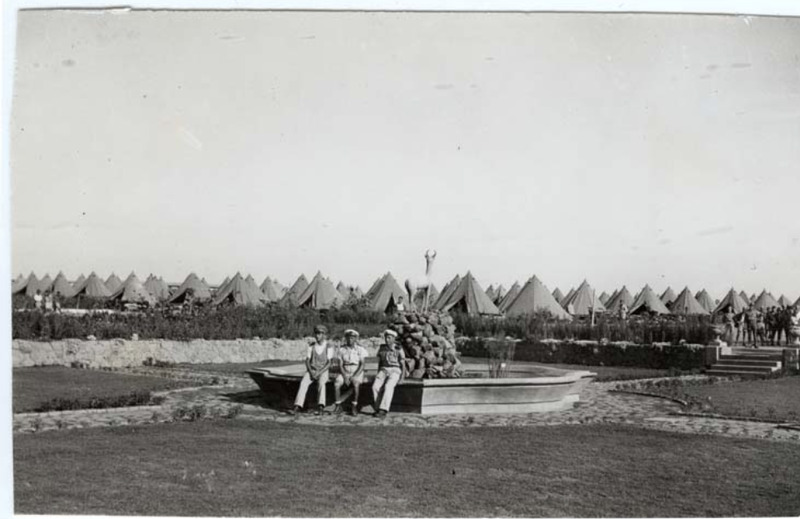 Zonderwater_9- 18 February 1943 - POW Camp - POW sitting on a fountain with camp in the backgroup.png